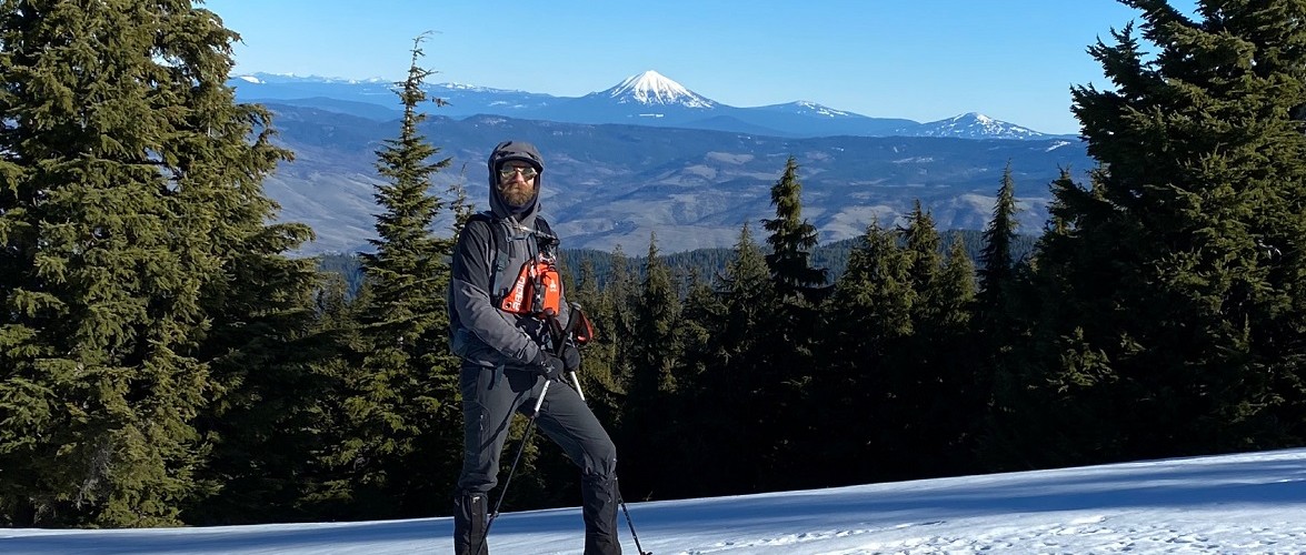 guide standing in the snow with mountains in the background and trees around