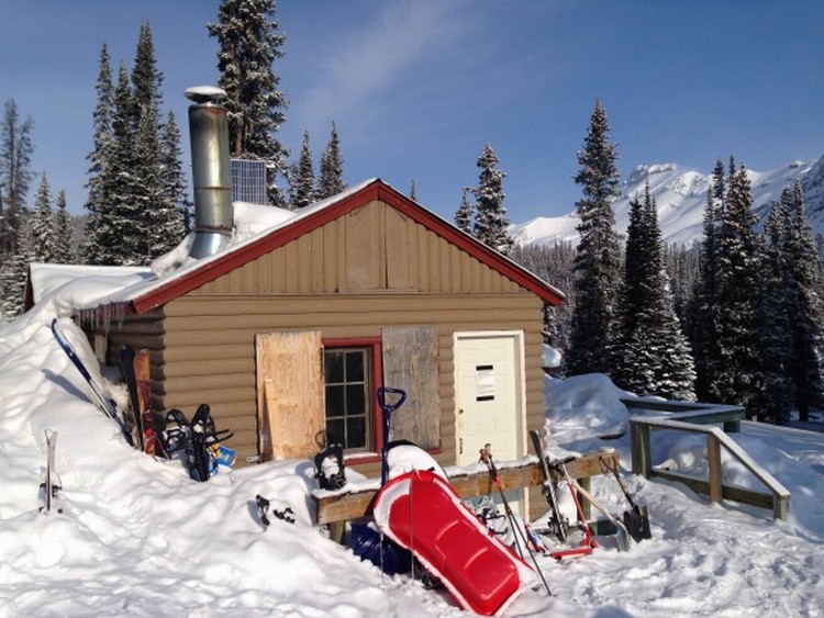 cabin with snow on roof and side with sled in foreground