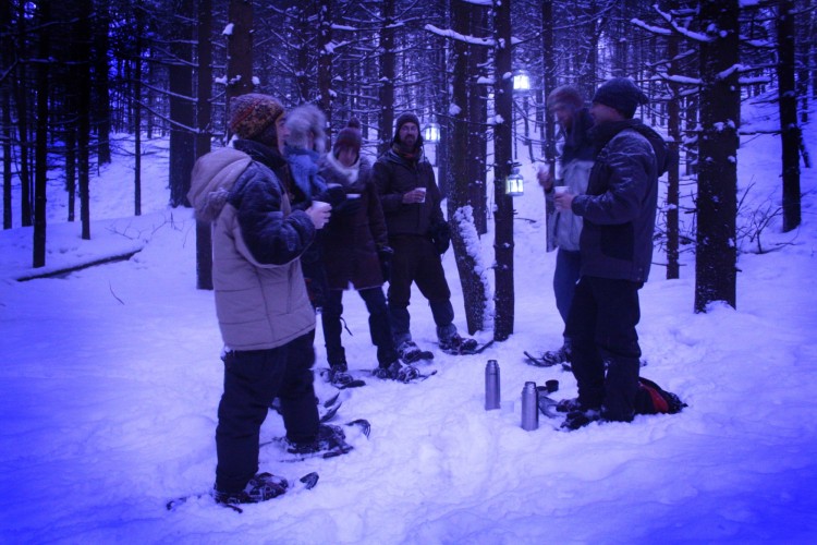 people on snowshoes gathered near trees at night sipping hot chocolate