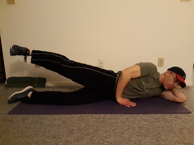 at home hip exercises: man lying on side on the ground demonstrating hip abduction exercise