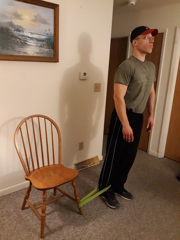 man standing next to chair demonstrating hip adduction exercise