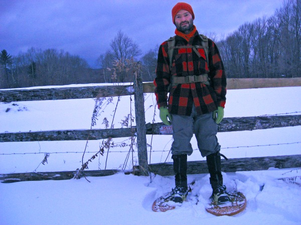 snowshoes for big people and heavy loads: man stands on wooden snowshoes with a backpack in front of fence