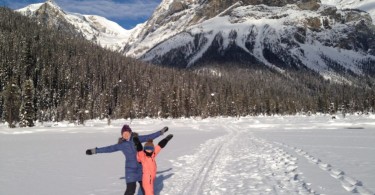 Woman and child standing in snow in front of mountain.