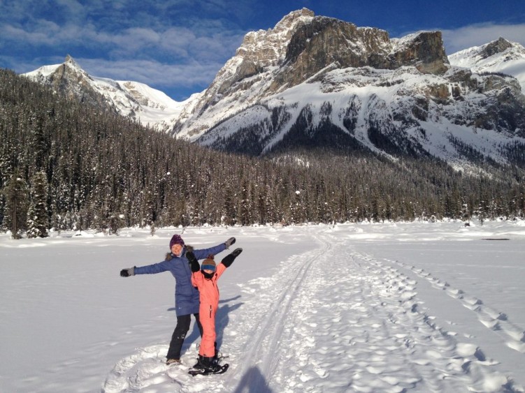 winter hiking with kids: Woman and child standing in snow in front of mountain.