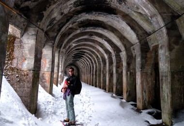 man posing with a dog on snowshoes in snow-filled tunnel