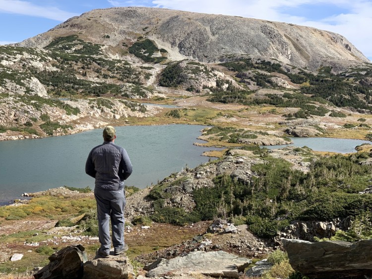 man looking out into distance on trail with lake in the fall