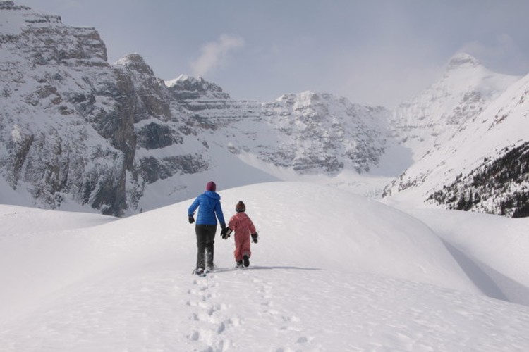 two people walking in snow with mountains in background