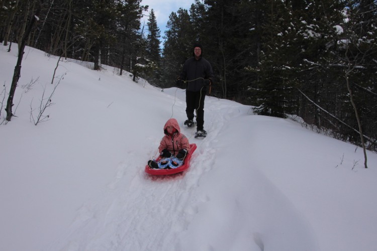 man guiding a sled with child in it down a snowy hill
