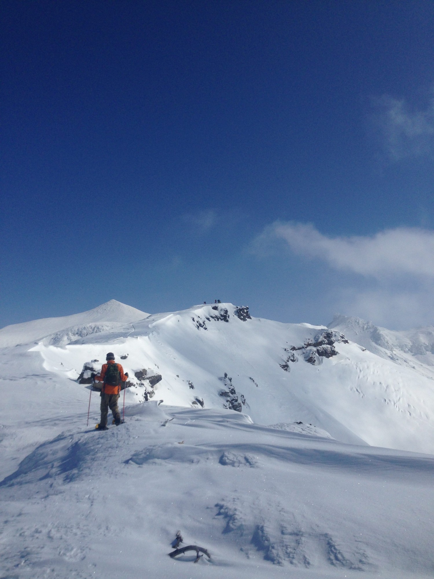 man walking on mountain peak with blue skies- Goodmacher