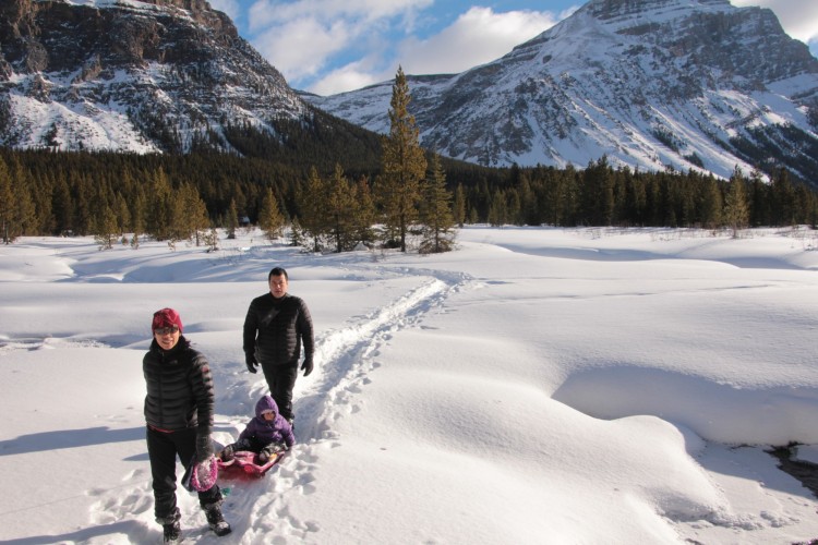 family pulling sled in deep snow with mountains in background