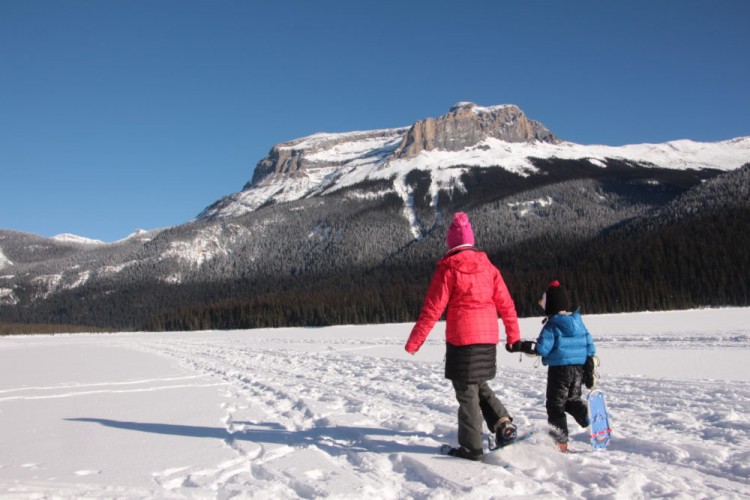 adult and child snowshoe across Emerald Lake hand in hand