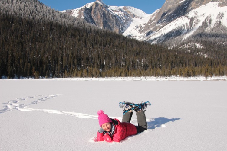 woman lying stomach down in snow with snowshoes propped up and posing for camera