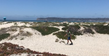 man in background using snowshoes on sand with ocean view in distance and dunes all around