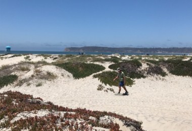 man in background using snowshoes on sand with ocean view in distance and dunes all around