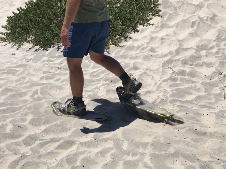 close up of snowshoes in sand while man is walking