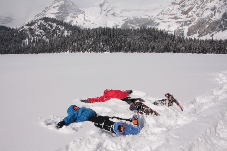 adult and child laying in the snow on snowshoes