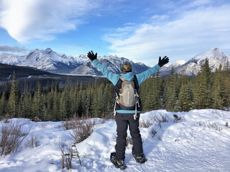 person on snowshoes looking at lake and mountains with arms outstretched