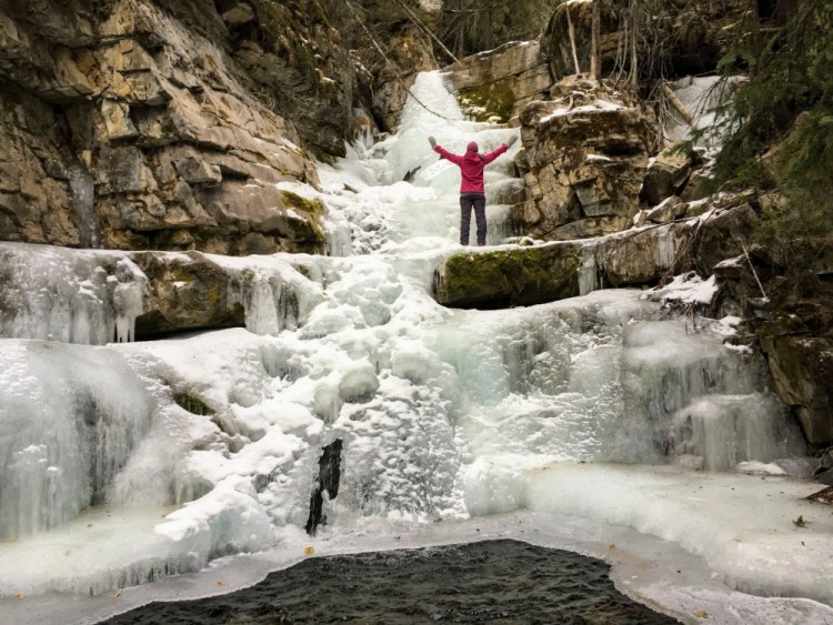 person standing with arms outstretched near top of Upper Falls, Kananaskis