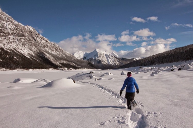 person snowshoeing in deep snow with mountains in background