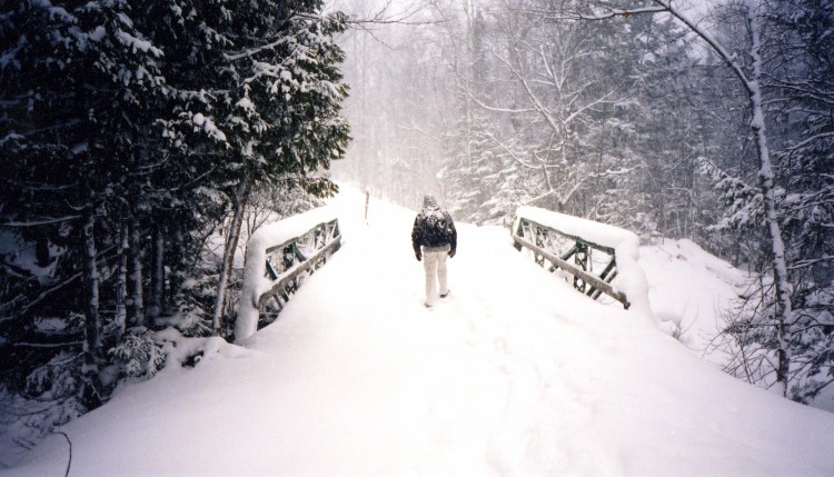 person snowshoeing in deep snow over bridge on trail in U.P Michigan