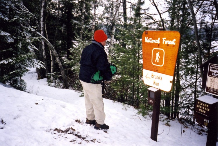 man on a snowy snowshoe trail surrounded by trees and signage in the UP of Michigan