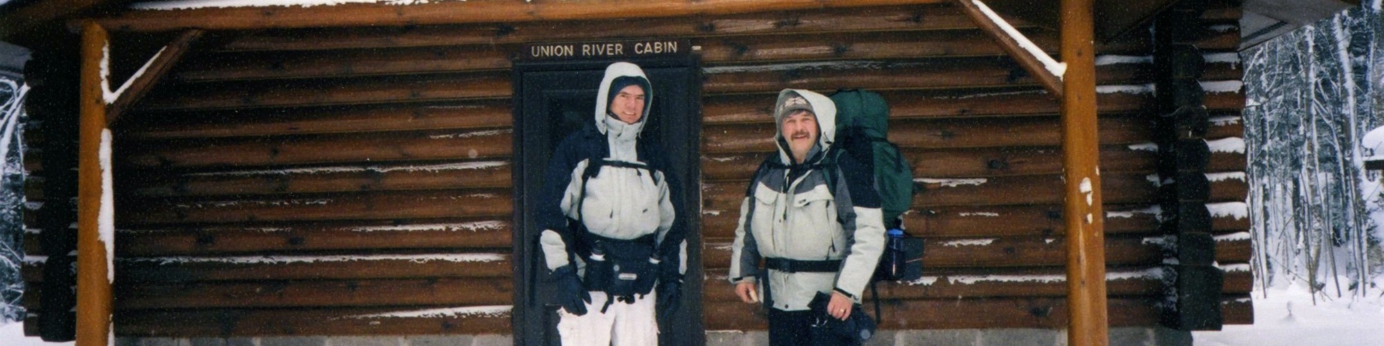 two men standing outside a log cabin in winter