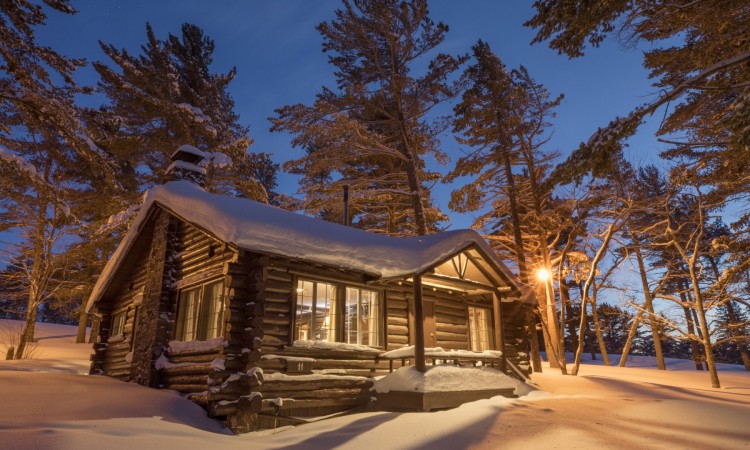 cabin covered in snow with trees and open sky in background