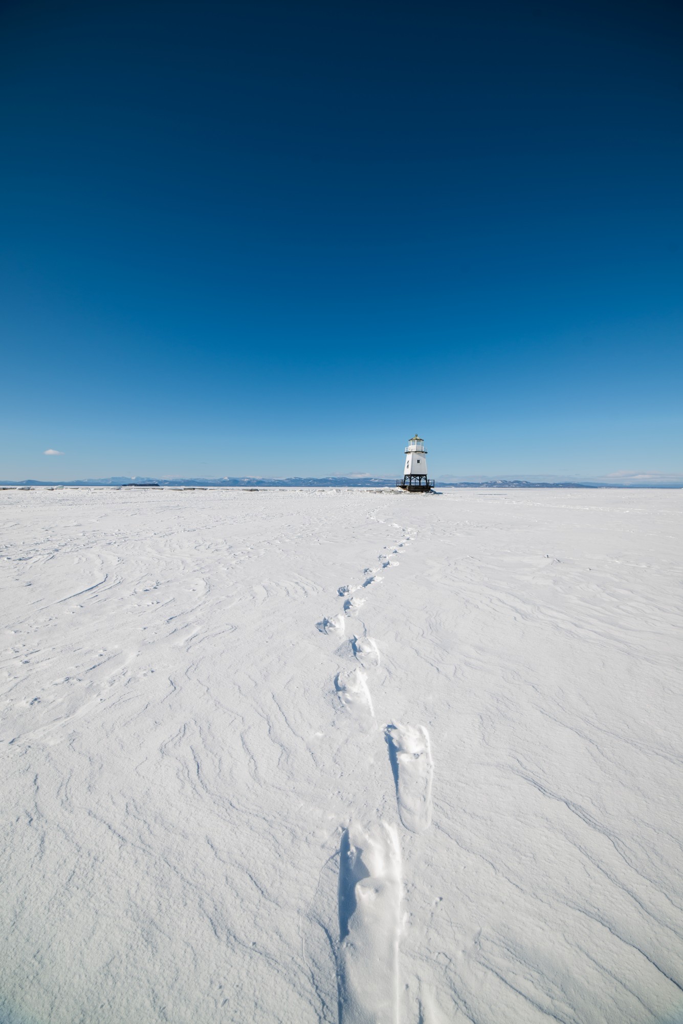 snowshoe tracks towards lighthouse under blue sky