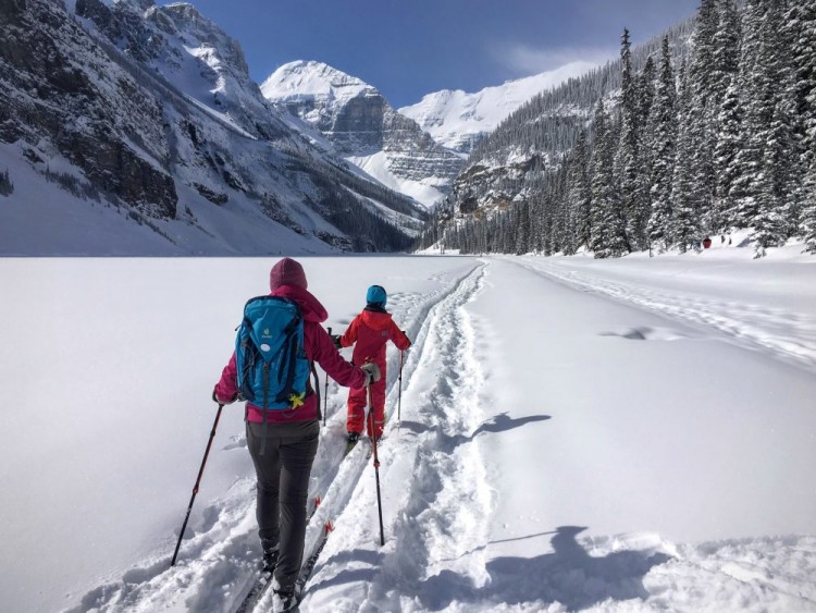 winter trail etiquette: two skiers on ski tracks with snowshoe tracks next to them (multi-use trail)