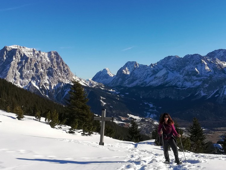 why hiking is good for you: snowshoer next to cross on mountain summit