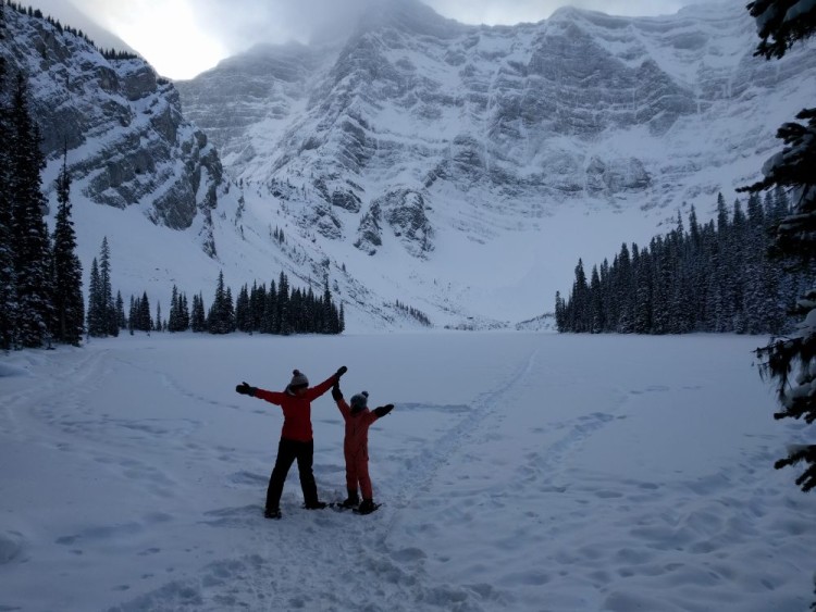 winter hiking with kids: mom and son on snow with arms raised and mountain in the background