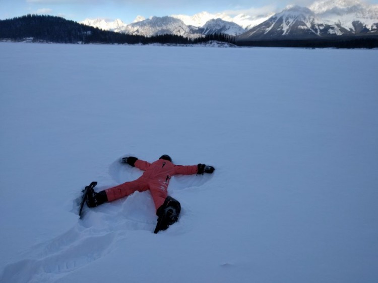 person lying with arms and legs spread out in the snow while wearing snowshoes