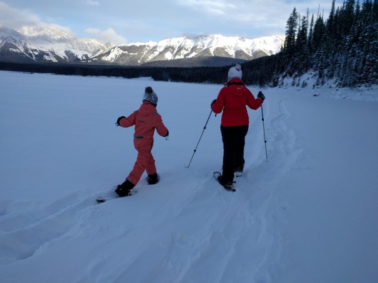 Adult and child snowshoeing with mountains in background