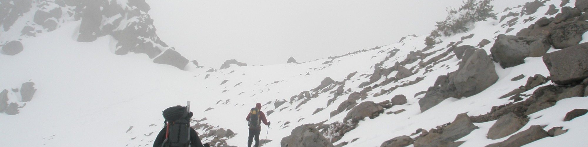 two people hiking a mountain with snow using snowshoes and poles