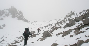 two people hiking a mountain with snow using snowshoes and poles