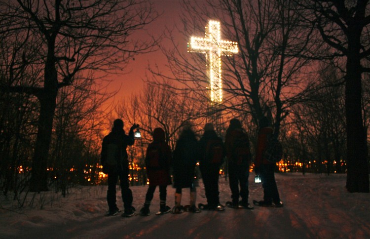 group of people on snowshoes standing beneath illuminated cross at night