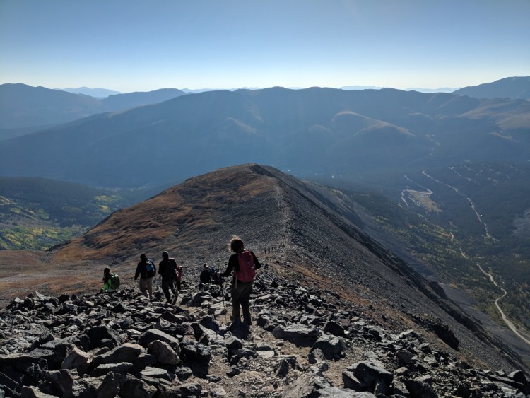 MSR DynaLock Explore Poles: people descending mountain summit with trail and blue sky in the background