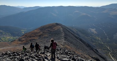 people descending mountain summit with trail and blue sky in the background
