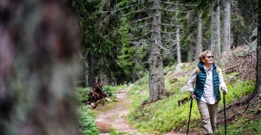 senior woman hiking on trail with nordic walking poles
