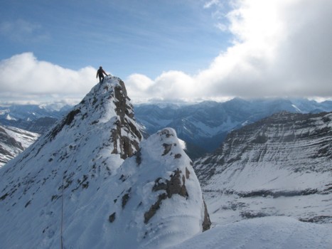 man sitting atop a mountain ridge with blue sky and clouds