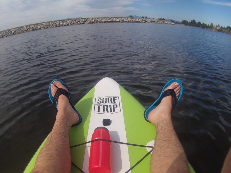 legs resting on paddleboard with water and rocks in background
