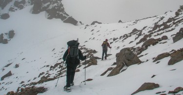 two people snowshoeing on the side of a mountain with poles and backpacks