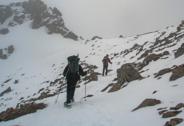 two people snowshoeing on the side of a mountain with poles and backpacks