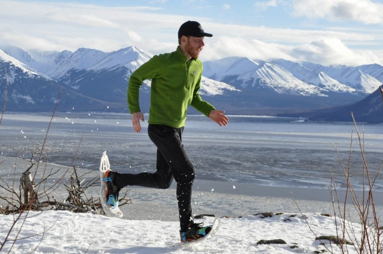 man running on snowshoes with mountains in background
