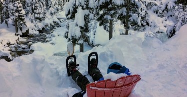 child sitting on a hill looking at a river on a chair in the snow