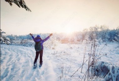Snowshoer on trail with open arms towards sunset
