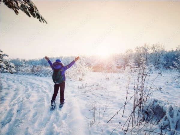 Snowshoer on trail with open arms towards sunset