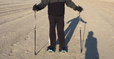 man posing with snowshoes and poles on sand