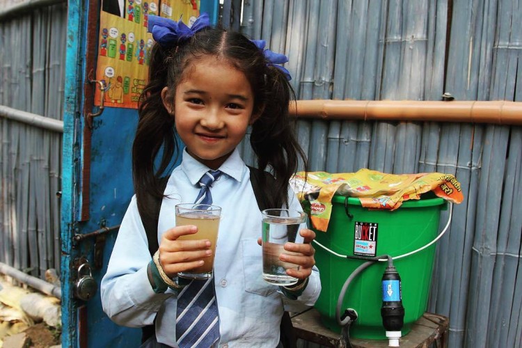 child holding clean and dirty water with Sawyer filter in background