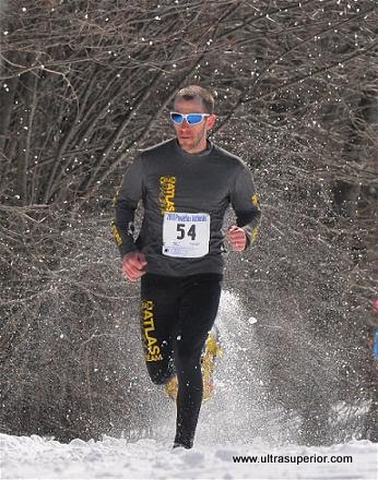 man racing in snowshoes with trees behind him